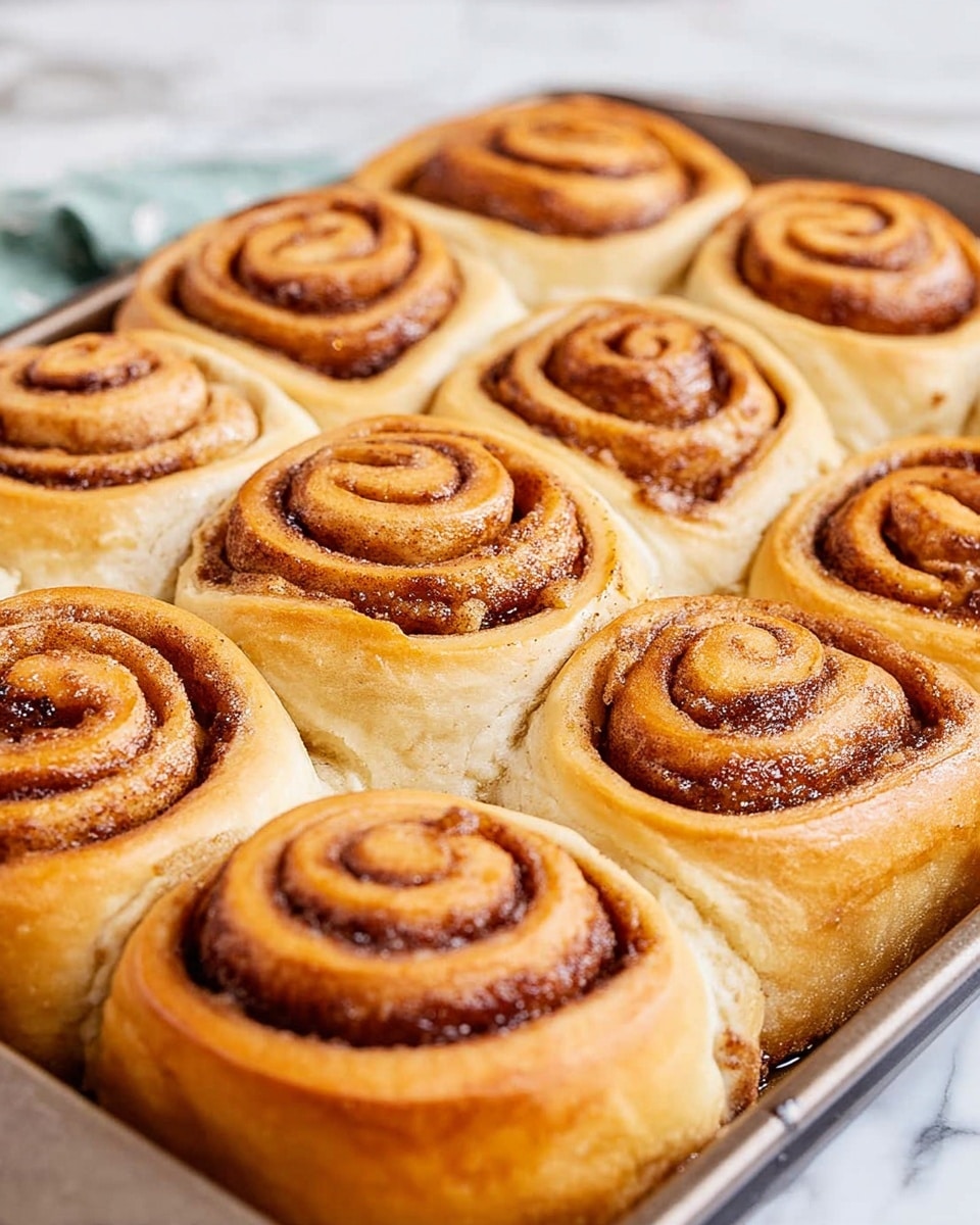 A single cinnamon roll sits in the middle of a white plate on a white marbled surface. The roll is thick and fluffy with three visible layers spiraling up from the base, showing a golden-brown dough with darker cinnamon spots in between. The top layer is coated with a smooth, shiny white glaze that trickles slightly down the sides, enhancing the soft texture. There are two thick pieces of the roll pulled away on both sides, showing the light, airy inside of the dough. A small pool of the same white glaze sits under the roll. Photo taken with an iphone --ar 4:5 --v 7