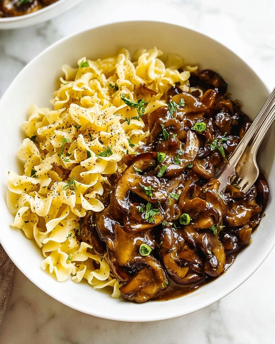 Two white bowls are placed on a white marbled surface, each filled with two layers; the bottom layer is light yellow, soft, and scrambled egg noodles with a folded, irregular texture, while the top layer is a glossy, dark brown mushroom sauce with sliced mushrooms and chopped green herbs sprinkled on top. Both bowls have a silver spoon inside, and a grey patterned cloth is loosely placed near the bowls. There are also two clear glasses of water present in the scene, with natural light highlighting the textures on the food. photo taken with an iphone --ar 4:5 --v 7