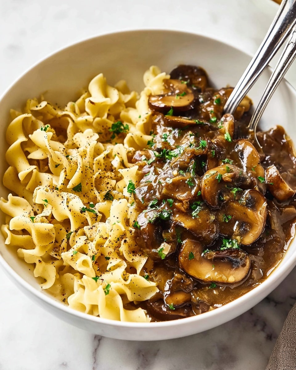 A white bowl containing two main layers: on the left side, soft, curly, pale yellow noodles with a light texture and specks of black pepper; on the right side, a glossy, rich brown mushroom sauce with visible sliced mushrooms and small green herb pieces sprinkled on top. Two silver forks rest inside the bowl on the left side. The bowl sits on a white marbled surface. photo taken with an iphone --ar 4:5 --v 7