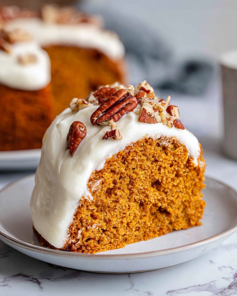 A single slice of orange-brown cake with a soft crumb texture sits on a white plate. The cake has one thick layer and is covered on top and sides with a thick layer of white frosting. There are several pieces of reddish-brown pecans placed on the frosting on top of the cake. The plate is set on a white marbled surface, and the background is softly blurred. photo taken with an iphone --ar 4:5 --v 7