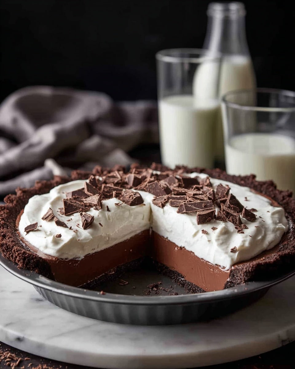 A chocolate pie sits on a white marbled surface, inside a dark metal pie pan. The bottom layer is a thick, smooth dark chocolate filling, topped by a fluffy white cream layer that covers the entire surface. The top cream layer is decorated with scattered small chunks of dark chocolate. A slice has been removed, revealing the even layers and creamy texture of the pie. In the background, a tall glass and a small bottle filled with milk are visible, with a dark backdrop. Photo taken with an iphone --ar 4:5 --v 7