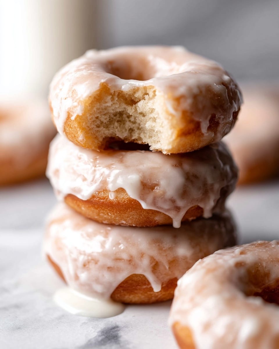 The image shows several round donuts with a thick white glaze covering most of their surfaces, sitting closely together on a white plate. Each donut has a rough, bumpy texture beneath the smooth glaze, showing a golden-brown color peeking through the icing in places. One donut at the front has a small piece broken off, revealing a soft, crumbly inside with the same golden-brown tone. The donuts have a hole in the middle and the glaze looks shiny and slightly uneven, enhancing their homemade look. The whole scene is set on a white marbled surface. photo taken with an iphone --ar 4:5 --v 7