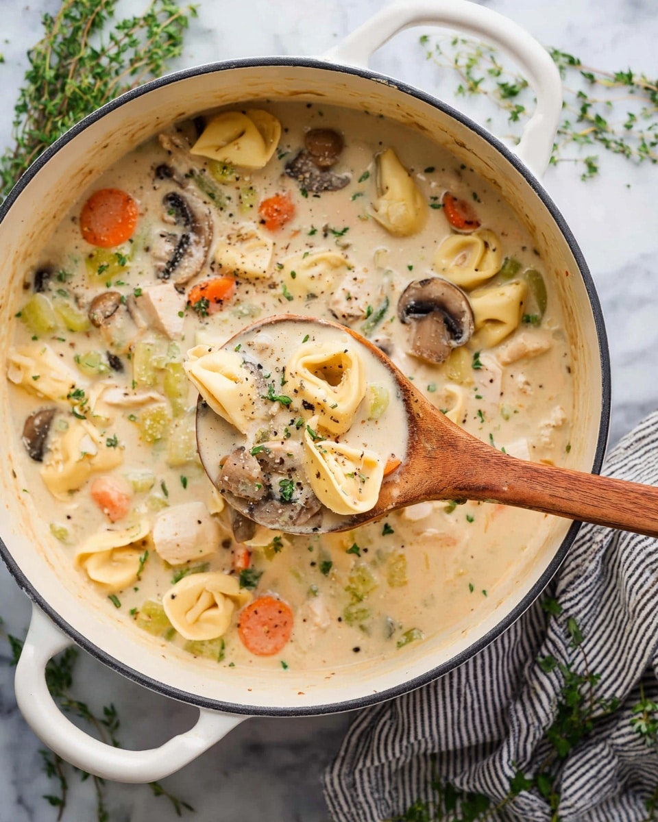 A white pot filled with creamy soup that has three main layers: a light beige creamy broth base with small herbs scattered throughout, a mix of soft, curved tortellini pasta pieces in pale yellow sitting throughout the soup, and colorful vegetable chunks including bright orange carrot slices, light green celery, and sliced brown mushrooms floating on top and inside the soup. A wooden spoon dipped in the soup lifts a portion showing pasta, vegetables, and some small pieces of chicken, all covered in the creamy broth with a sprinkle of green herbs on top. The pot is on a white marbled surface with a striped cloth and green herb sprigs partly visible around it. photo taken with an iphone --ar 4:5 --v 7