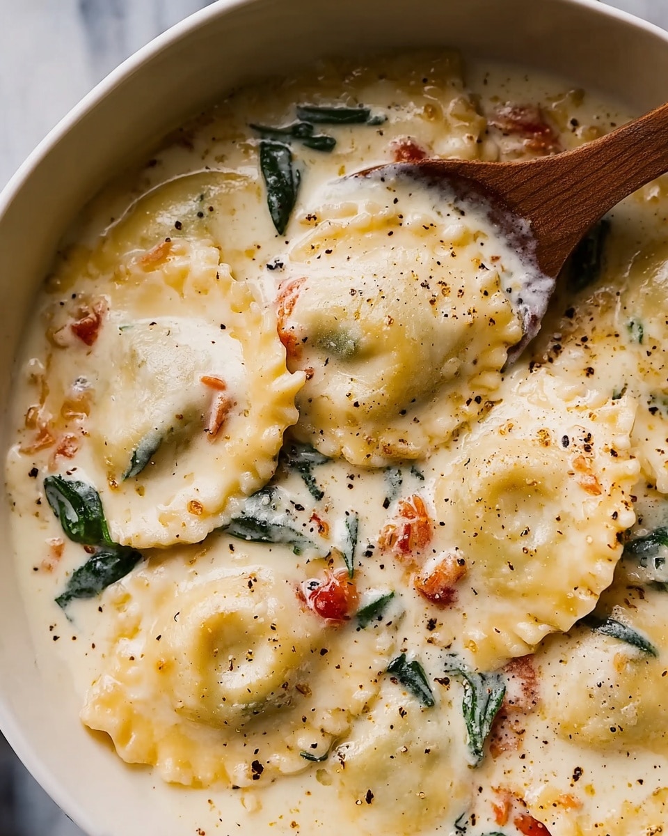 The image shows a close-up of a white pot filled with a creamy sauce covered with tortellini pasta. The sauce is light yellow with visible bits of green spinach and small pieces of red sun-dried tomatoes mixed throughout. The tortellini are plump, round, and slightly folded, sitting evenly coated in the thick sauce. There is a sprinkle of black pepper on top, adding specks of dark contrast against the light cream sauce. The background is a white marbled texture. Photo taken with an iphone --ar 4:5 --v 7