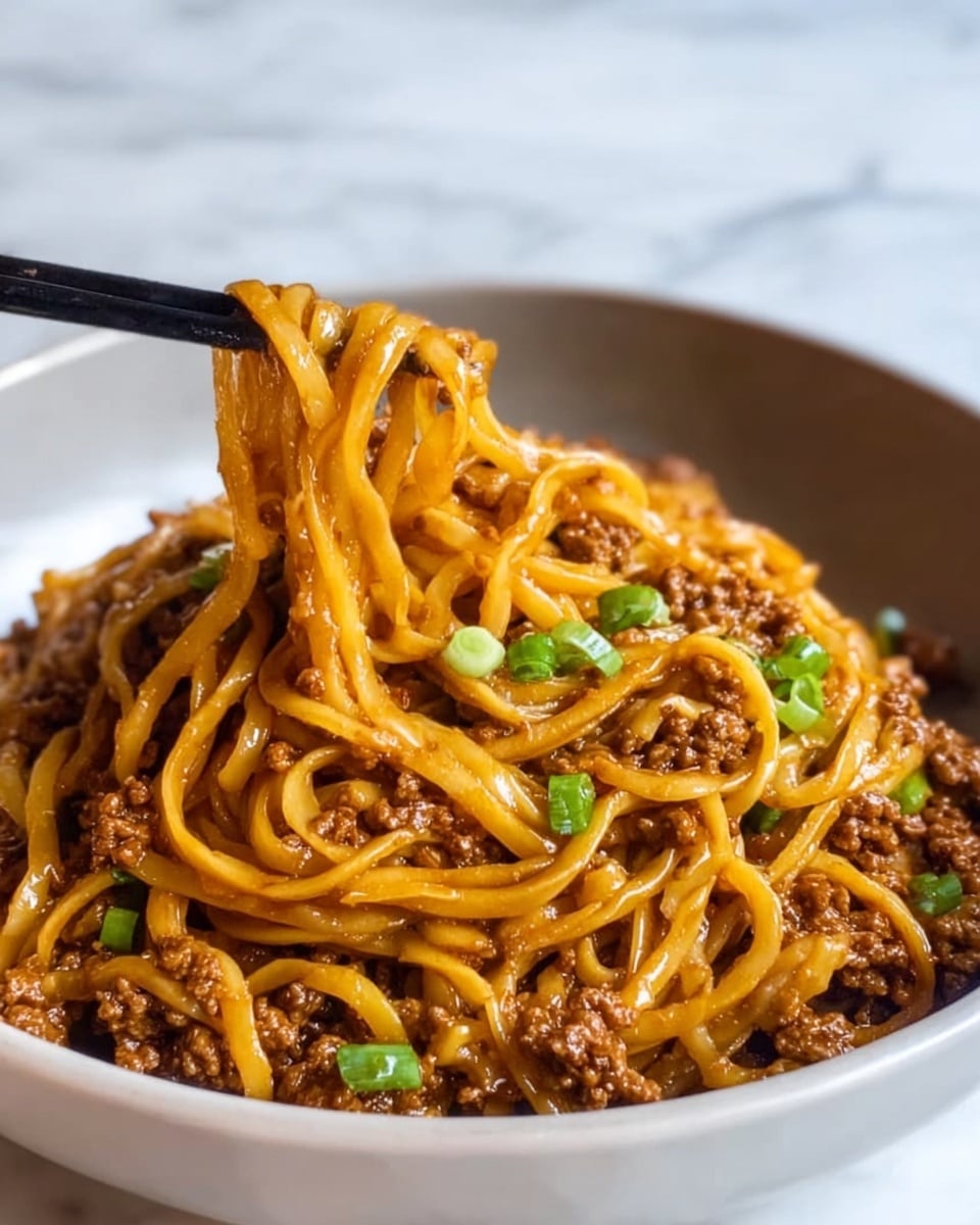 Large white serving bowl filled with a generous portion of savory Asian-style noodles tossed with ground beef, garnished with chopped green onions and finely diced vegetables, glistening with a rich, savory sauce, presented as a full, hearty serving, photographed from a close 3/4 angle on a white marble surface with natural lighting, professional food styling photo taken with an iphone --ar 4:5 --v 7