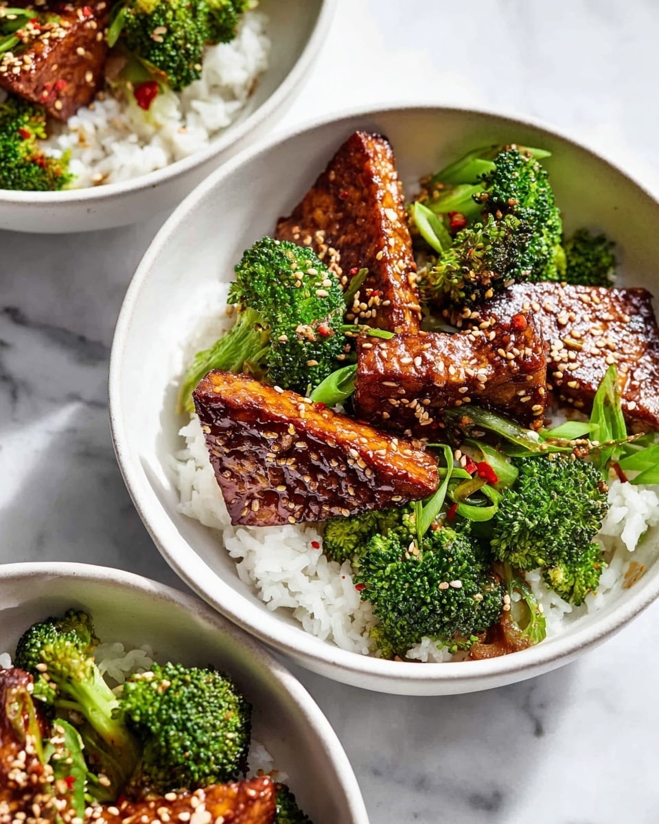 Large white serving bowls filled with a vibrant arrangement of steamed broccoli florets, fluffy white rice, and multiple glossy, richly glazed tempeh triangles sprinkled generously with toasted sesame seeds and chili flakes, whole dishes photographed from a 3/4 angle on a white marble countertop with natural lighting, professional food magazine hero shot, photo taken with an iphone --ar 4:5 --v 7