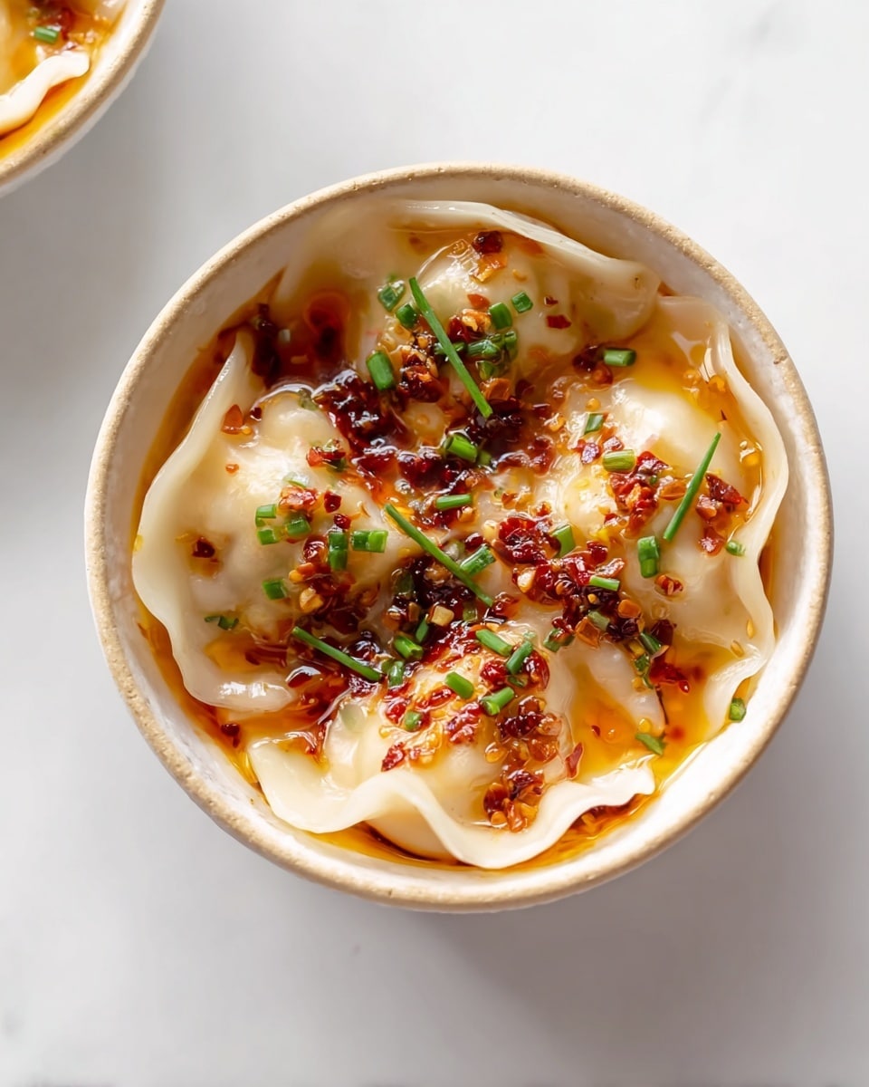 Large white serving dish filled with a generous portion of steaming hot wonton soup, featuring numerous smooth, plump wontons nestled in a clear, flavorful broth, garnished with scattered pieces of crispy fried shallots and finely chopped fresh chives, whole dish photographed at a 3/4 angle on a white marble countertop, illuminated with natural lighting for a professional food magazine hero shot, photo taken with an iphone --ar 4:5 --v 7