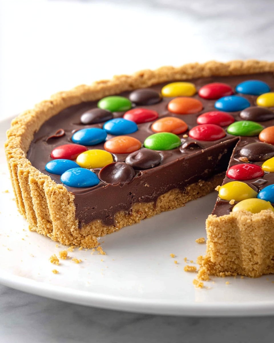 Whole round chocolate tart with a golden graham cracker crust, topped with a glossy dark chocolate ganache and scattered colorful candy-coated chocolate eggs in vibrant shades of blue, red, orange, yellow, white, cream, and green, arranged evenly across the surface, presented on a large white plate, photographed from a 3/4 angle with natural lighting on a white marble background, capturing the entire uncut tart in a professional food magazine hero shot style, photo taken with an iphone --ar 4:5 --v 7