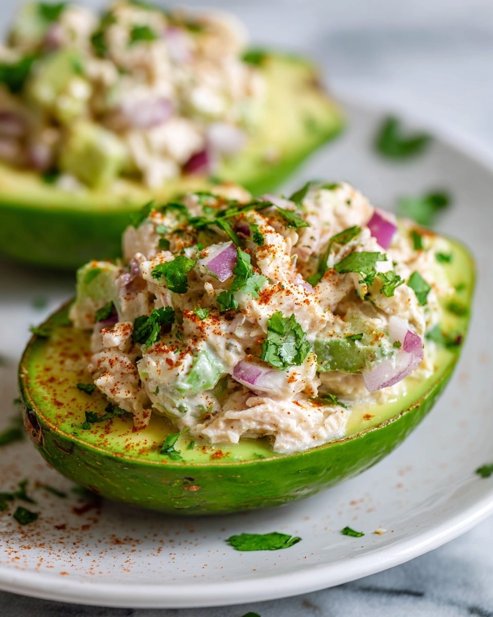 Multiple white plates arranged with whole ripe avocados halved and filled generously with creamy crab salad mixed with finely diced red onions and herbs, each avocado half sprinkled with chili powder and garnished with fresh cilantro, accompanied by lime wedges on a white marble countertop, photographed at a 3/4 angle with natural lighting, professional food magazine style photo taken with an iphone --ar 4:5 --v 7