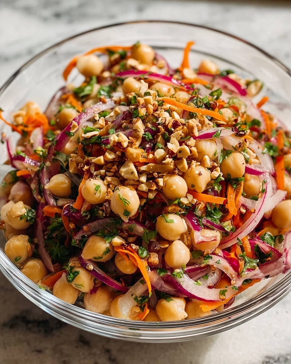 Large white bowl filled with a vibrant chickpea salad featuring whole chickpeas, thinly sliced purple onions, julienned orange carrots, chopped red chili flakes, and finely chopped fresh herbs, all tossed together with a light dressing and sprinkled with crushed nuts, the entire salad showcased from a professional 3/4 angle shot on a white marble countertop with natural lighting, a fresh and colorful presentation like a food magazine hero shot, photo taken with an iphone --ar 4:5 --v 7