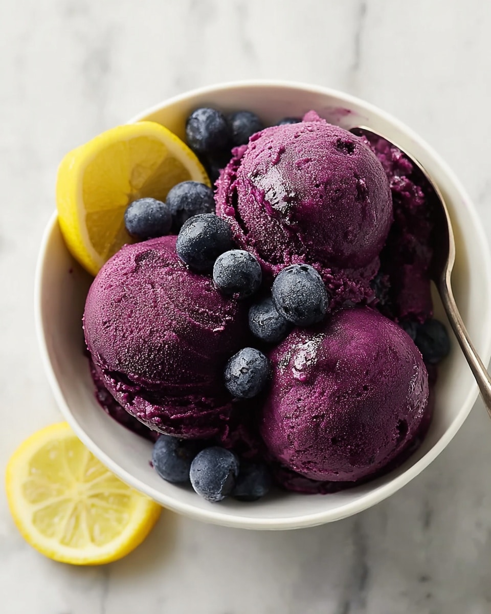Large white bowl filled with several scoops of vibrant deep purple blueberry sorbet, garnished with fresh whole blueberries and a slice of bright yellow lemon on the side, arranged on a white marble countertop, professional overhead food styling shot with natural lighting, whole dish in frame, hero food magazine style photo taken with an iphone --ar 4:5 --v 7