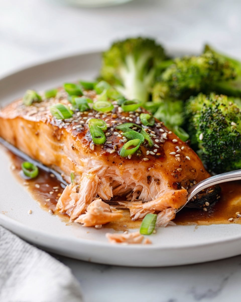 Large white oval serving platter featuring a whole perfectly glazed teriyaki salmon fillet topped with toasted sesame seeds and sliced green onions, surrounded by vibrant roasted broccoli florets with a glossy teriyaki sauce drizzle, presented on a white marble countertop with natural lighting from a 3/4 angle, styled like a hero food magazine shot, photo taken with an iphone --ar 4:5 --v 7