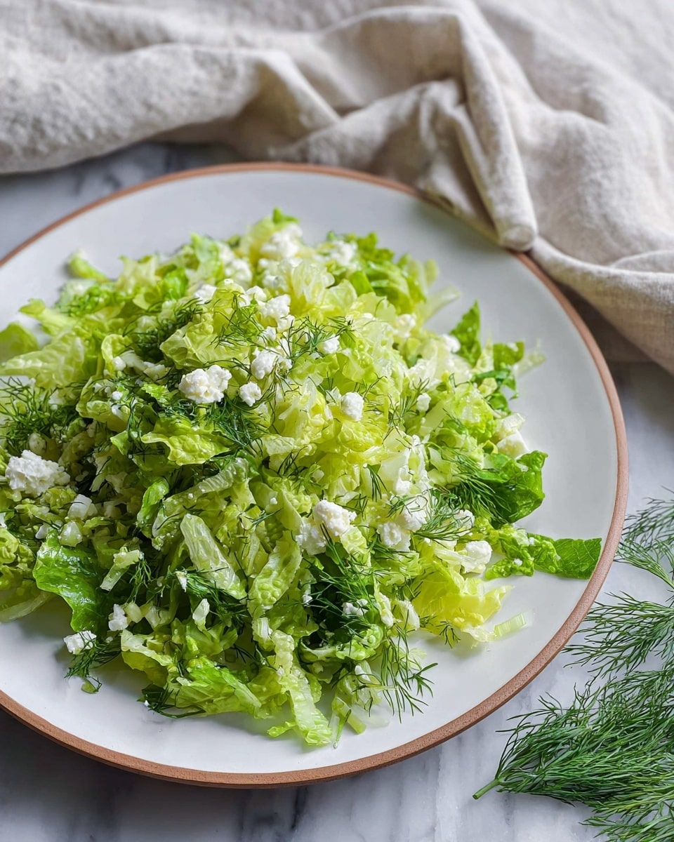 Large white bowl filled with a fresh green chopped salad featuring finely shredded lettuce, scallions, and crumbled feta cheese, garnished with sprigs of dill, accompanied by lemon halves and fresh dill on a white marble countertop, whole dish shown from a 3/4 angle with natural lighting, professional food styling photo taken with an iphone --ar 4:5 --v 7