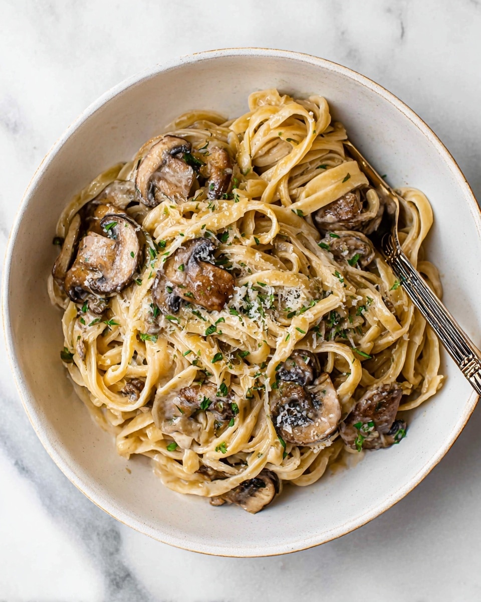 Large white bowl filled with creamy mushroom pasta made with thick linguine noodles tossed in a rich, silky sauce, whole sautéed mushroom caps nestled throughout, garnished with fresh herbs and a light sprinkle of grated cheese, the entire dish beautifully presented on a white marble countertop with natural lighting, professional food magazine hero shot photo taken with an iphone --ar 4:5 --v 7
