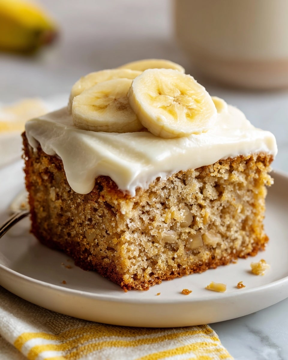 A large white rectangular baking pan filled with a whole freshly baked banana cake topped with a smooth layer of creamy frosting, each square section evenly iced and adorned with a single round banana slice on top, the cake showing a moist and tender crumb, presented on a white marble countertop with natural lighting in a professional food magazine style, photo taken with an iphone --ar 4:5 --v 7