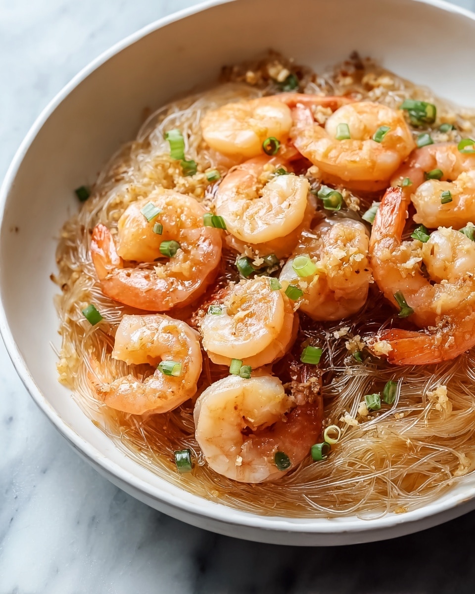 Large white serving bowl filled with a complete serving of sautéed shrimp atop translucent glass noodles, garnished with finely chopped green onions and a light savory sauce, showcasing the full dish with multiple plump shrimp arranged evenly over the noodles, photographed at a 3/4 angle on a white marble countertop with natural lighting, styled as a professional food magazine hero shot, photo taken with an iphone --ar 4:5 --v 7